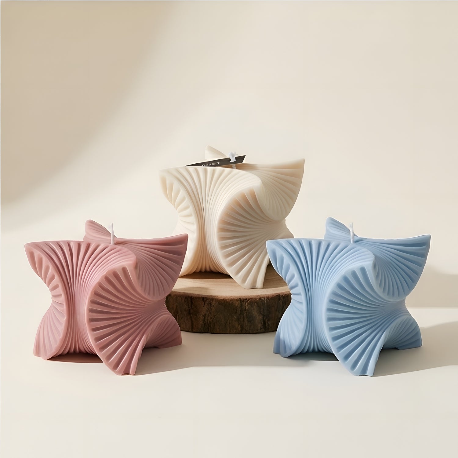 Sculpted decorative candles in cream, pink, and blue with modern geometric design on neutral background
