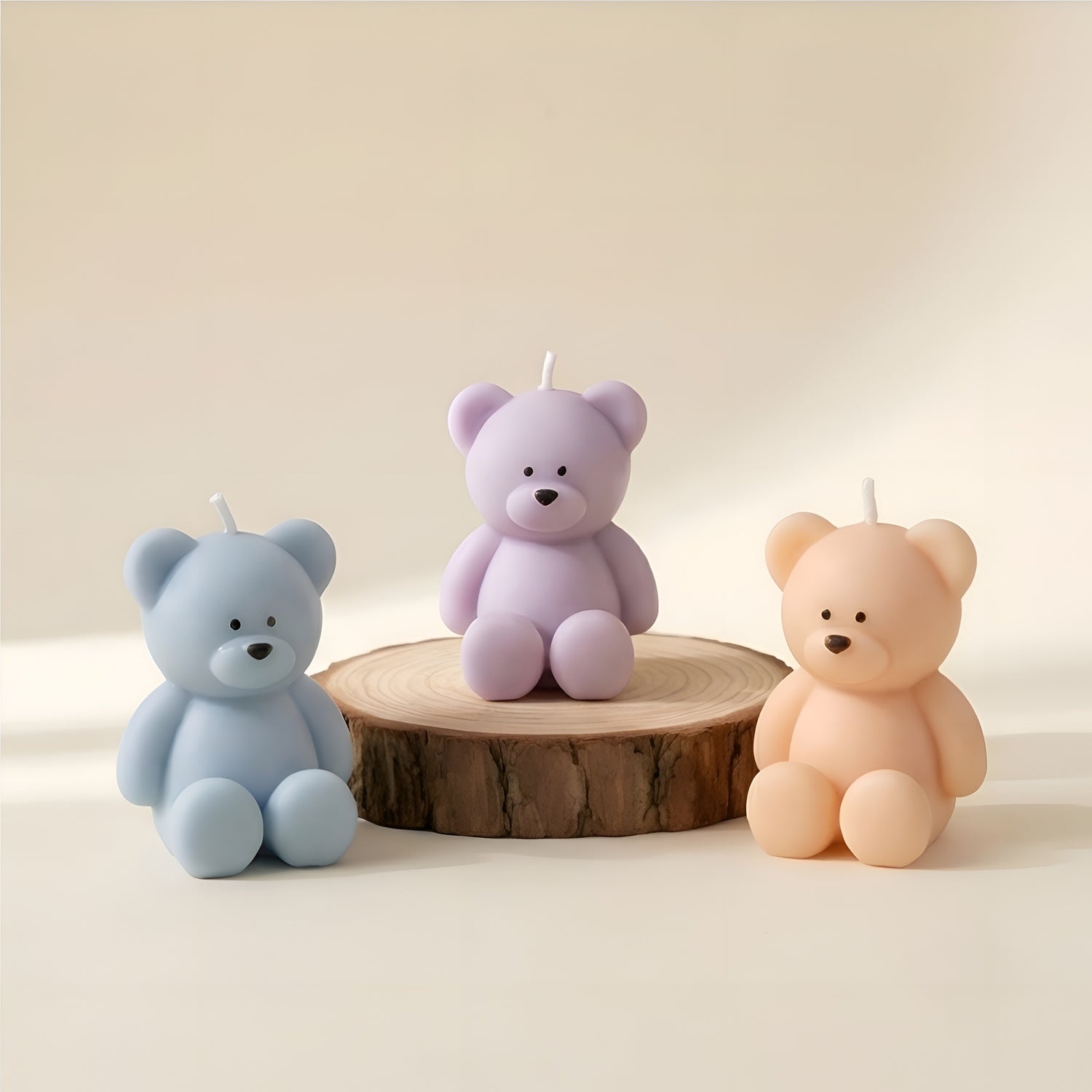 Three pastel teddy bear shaped candles, blue, purple, and peach, on light wood slab